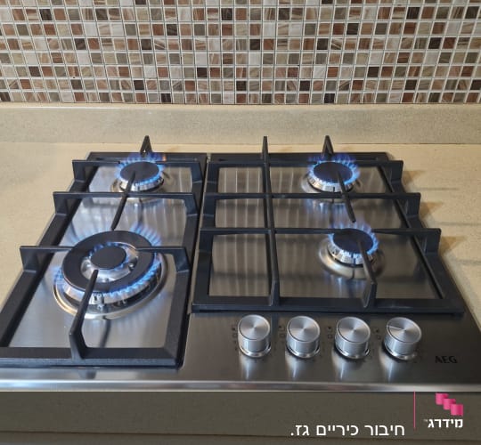 כיריים גז מנירוסטה מותקנות במטבח עם ארבעה מבערים דולקים